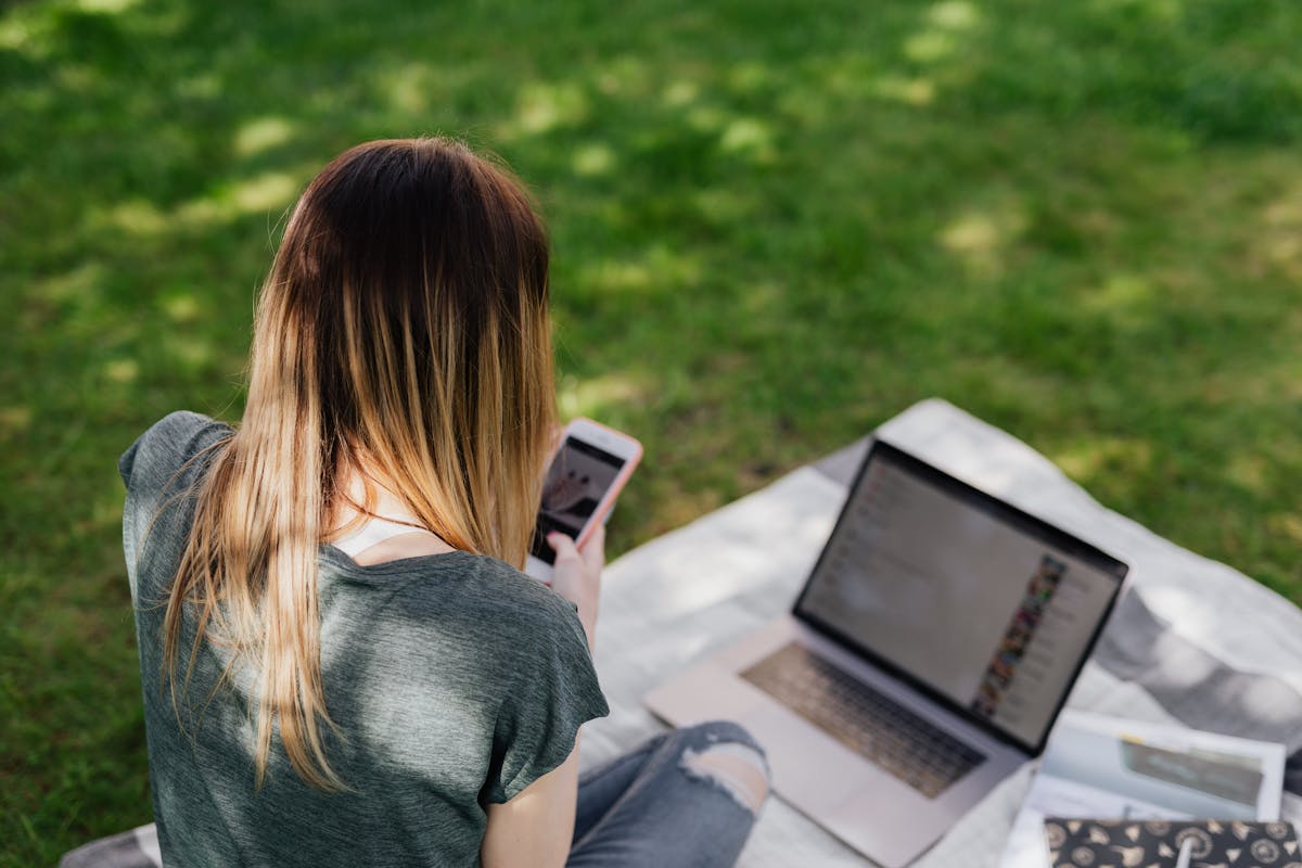 A teenager sitting in a park looking at a smartphone