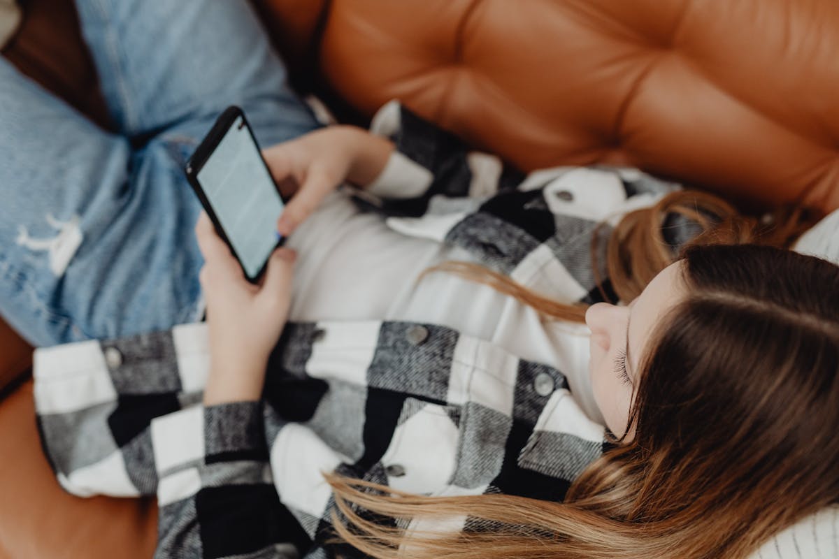 A teenage girl sitting on a sofa scrolling on her smartphone